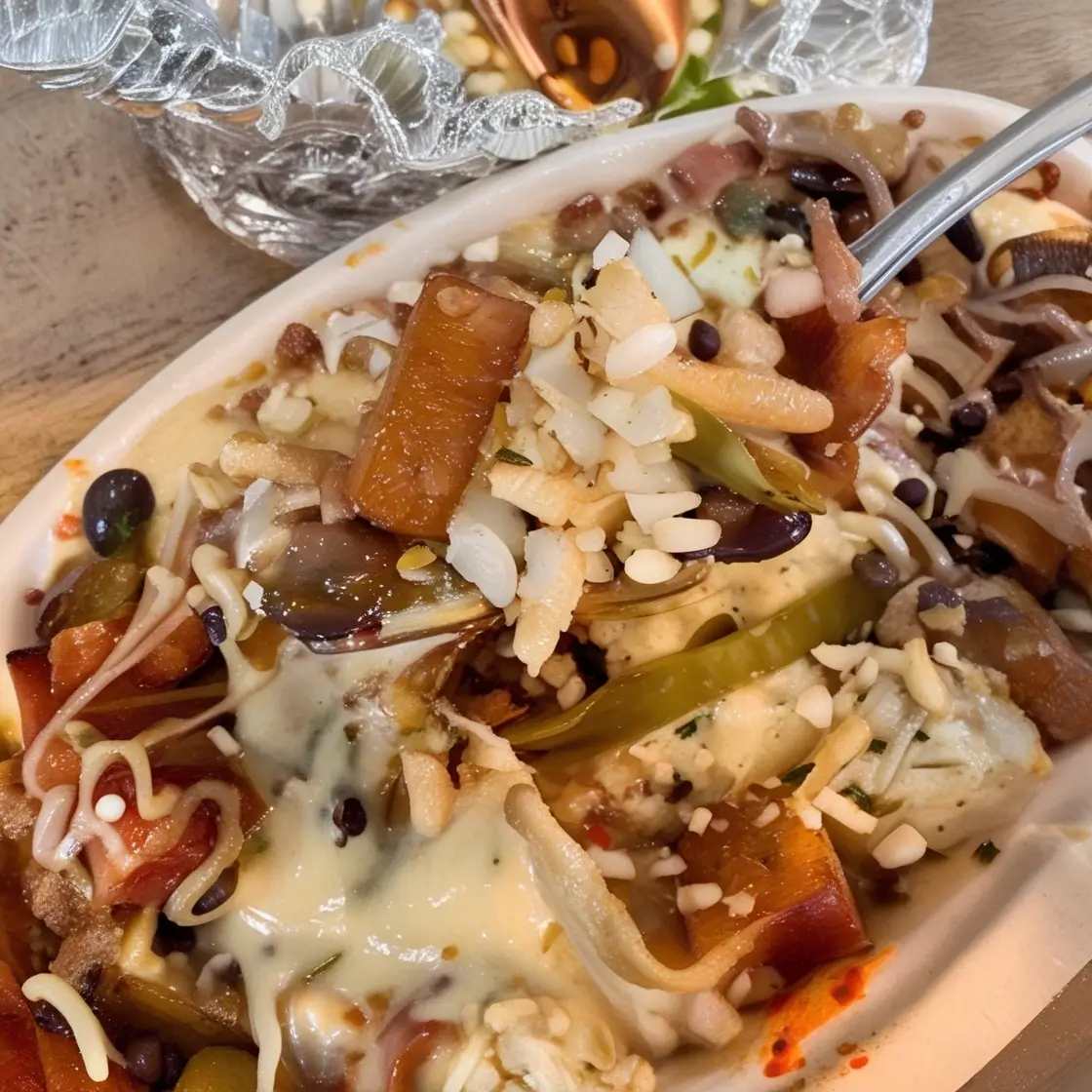 A close-up of a vibrant and colorful dish featuring creamy sauce, rice, black beans, sautéed vegetables, and melted cheese, garnished with seasonings.