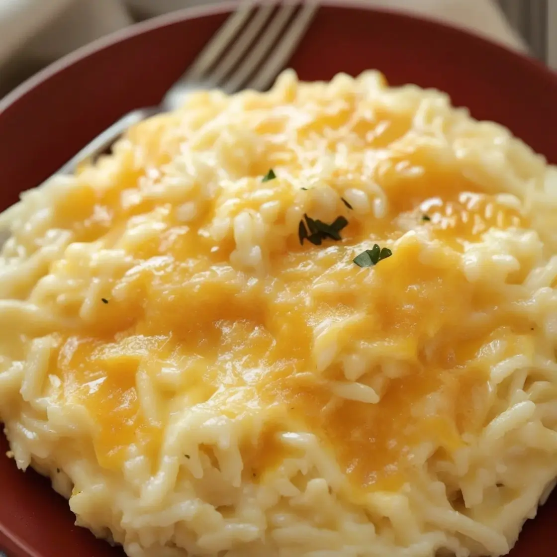 A plate of creamy and cheesy rice topped with melted cheddar cheese and garnished with fresh parsley.