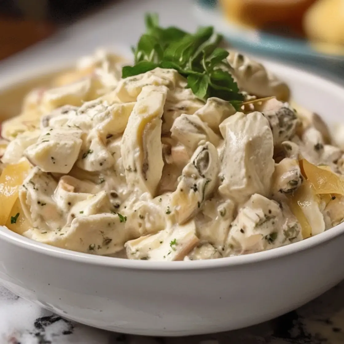 A bowl of creamy chicken salad garnished with fresh parsley on top, featuring tender chunks of chicken coated in a rich, seasoned dressing.